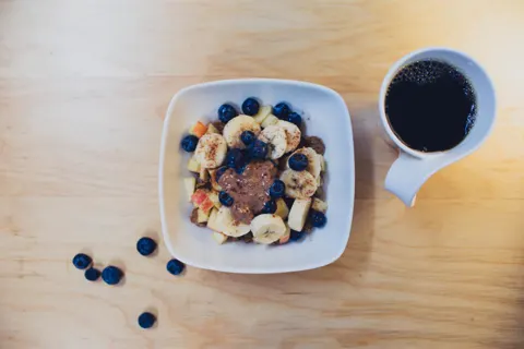 Tigela com banana e frutas vermelhas ao lado de uma xícara de café