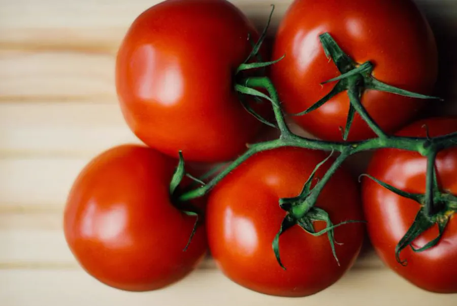 Tomates vermelhos com o cacho sobre uma mesa de madeira